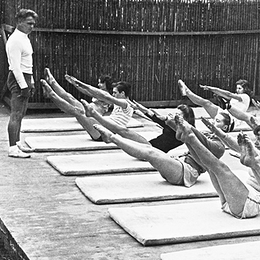 Joseph Pilates teaching the teaser exercise to a group of dancers outdoors