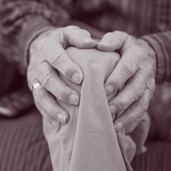 An old mans hands grip his sore knee. Maybe a healthcare problem solver could help?